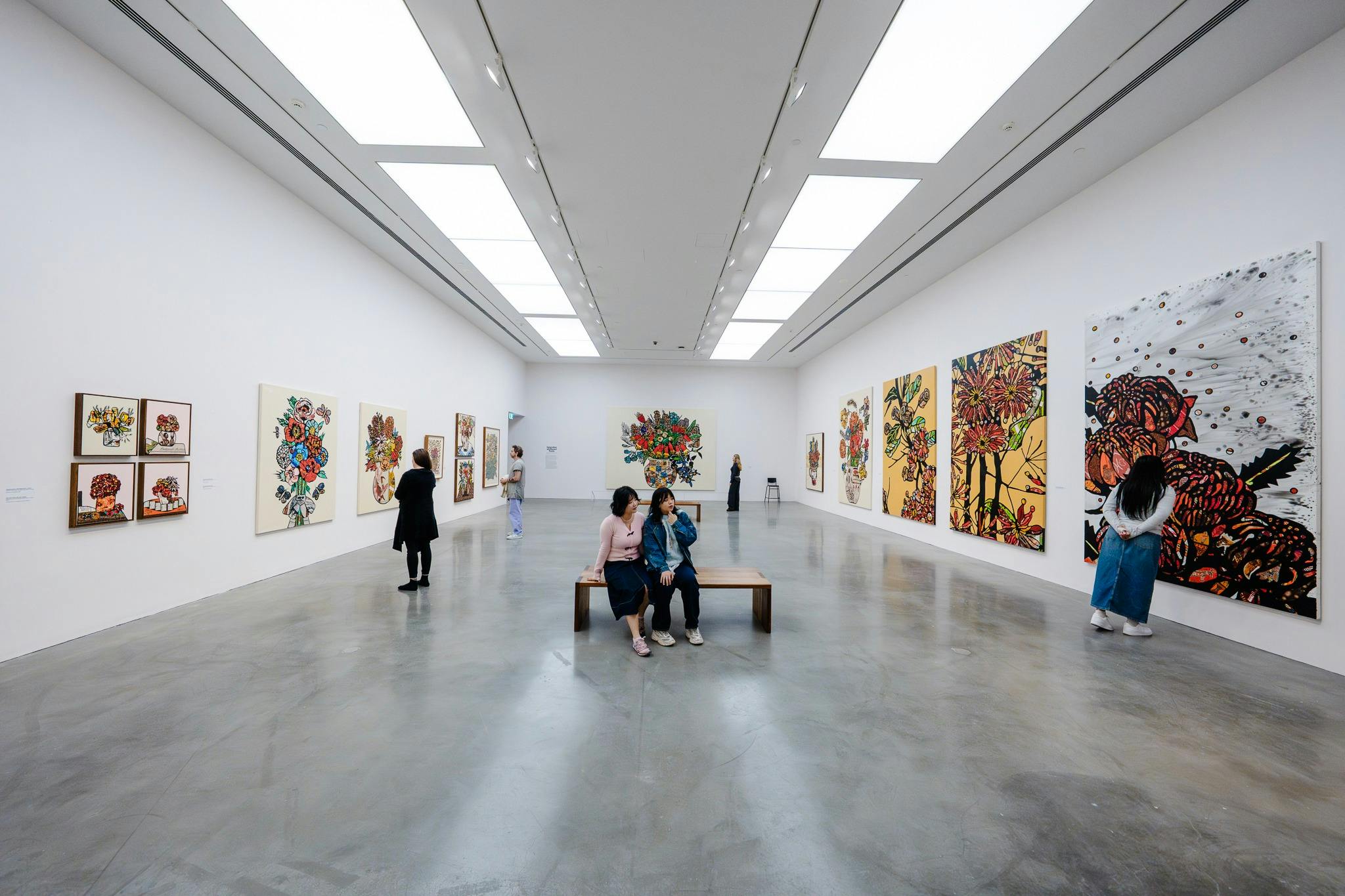 A wide shot of an art gallery with several large, colourful paintings on display.