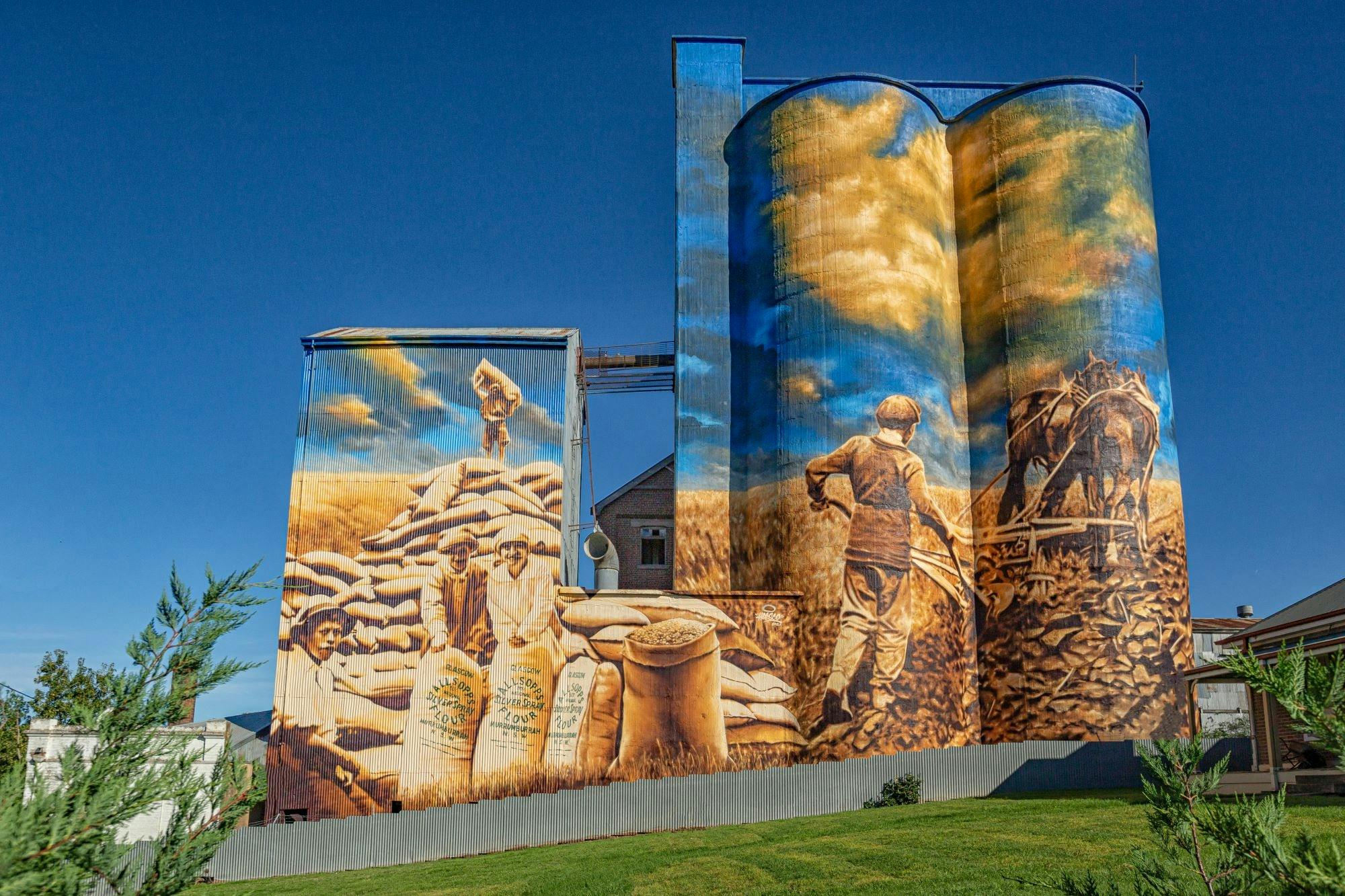 Murrumburrrah Silo Art depicting farmers handling sacks of flour and one tilling the soil by horse.
