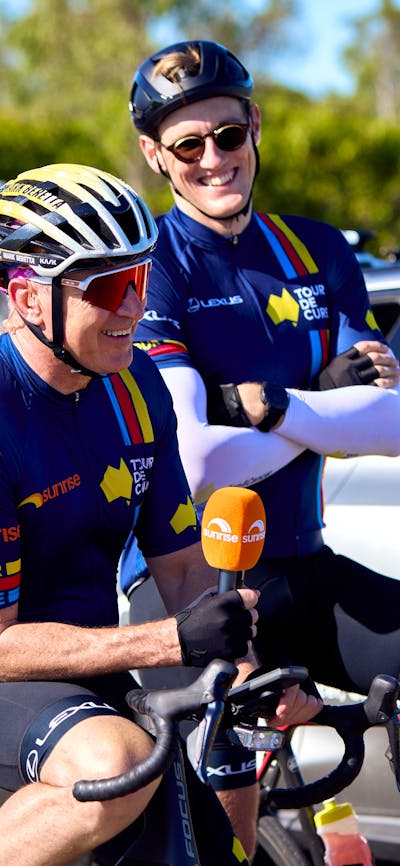Mark Beretta and Mack Horton casually sitting on their bikes in cycle kit during Signature Tour '25