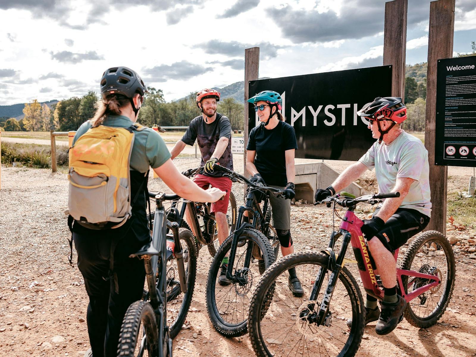 A group of riders stands facing a bike coach in front of a black sign that says Mystic