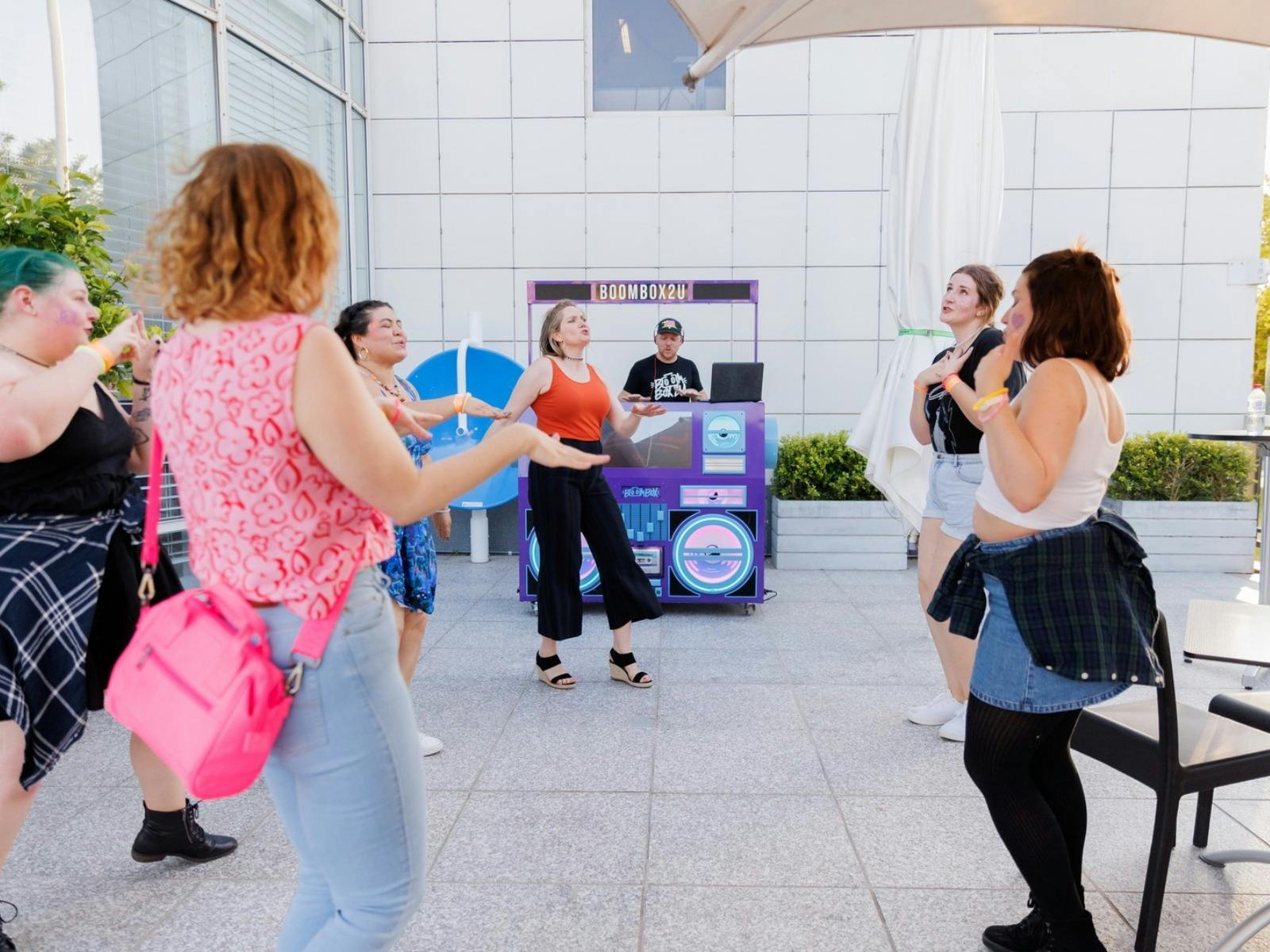A group of people dancing in front of a DJ - Boom Box 2 U