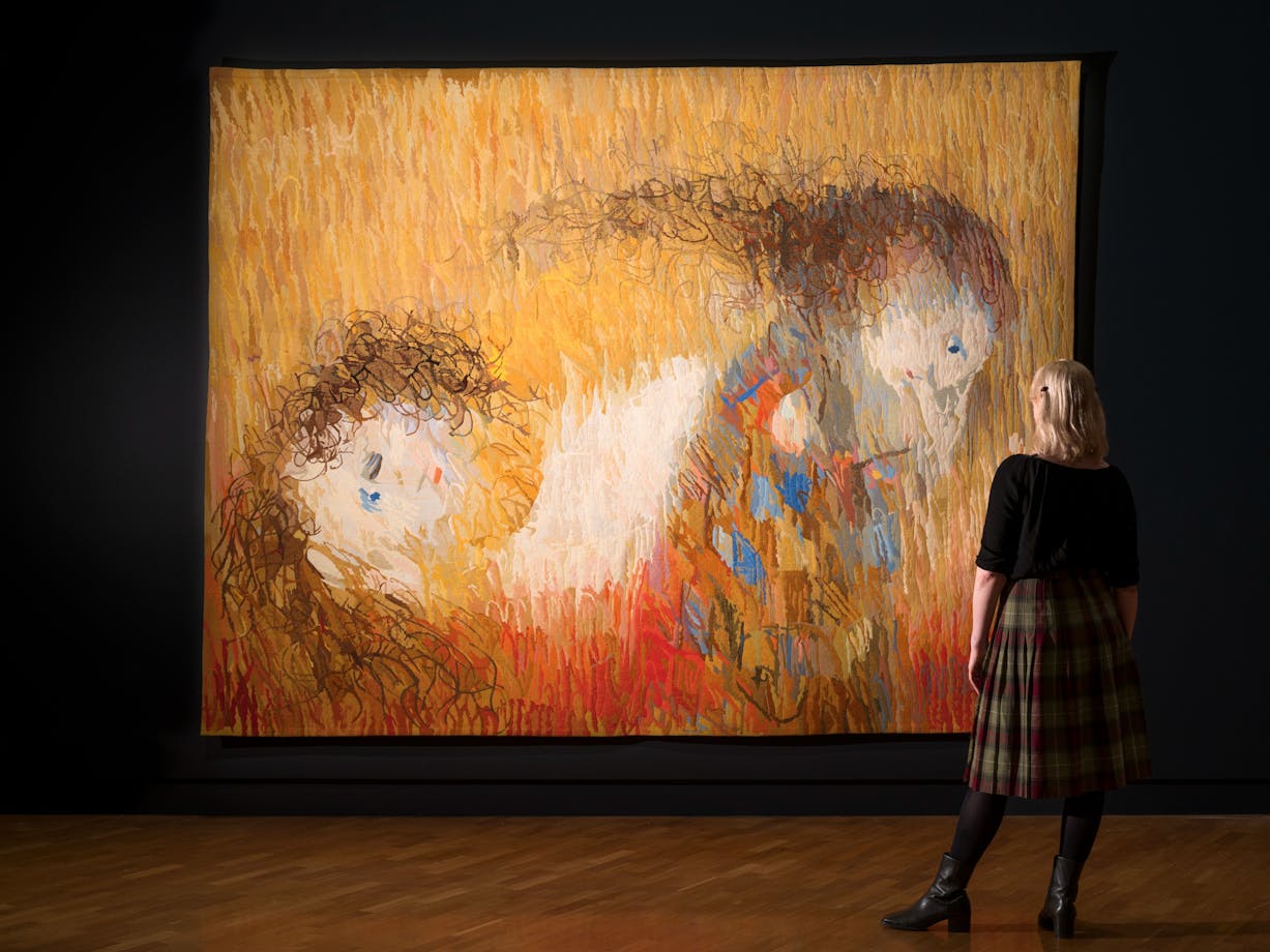 View of inside art exhibition with large tapestry and a visitor