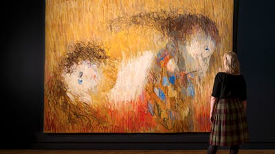View of inside art exhibition with large tapestry and a visitor
