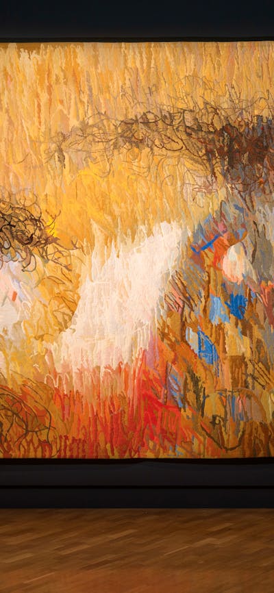 View of inside art exhibition with large tapestry and a visitor