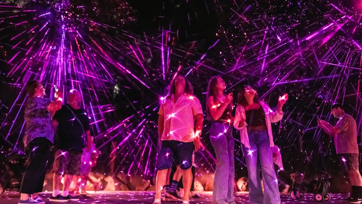 Group of people looking up, standing in the centre of pink and purple laser lights. Group of people looking up, standing in the centre of pink and purple laser lights.