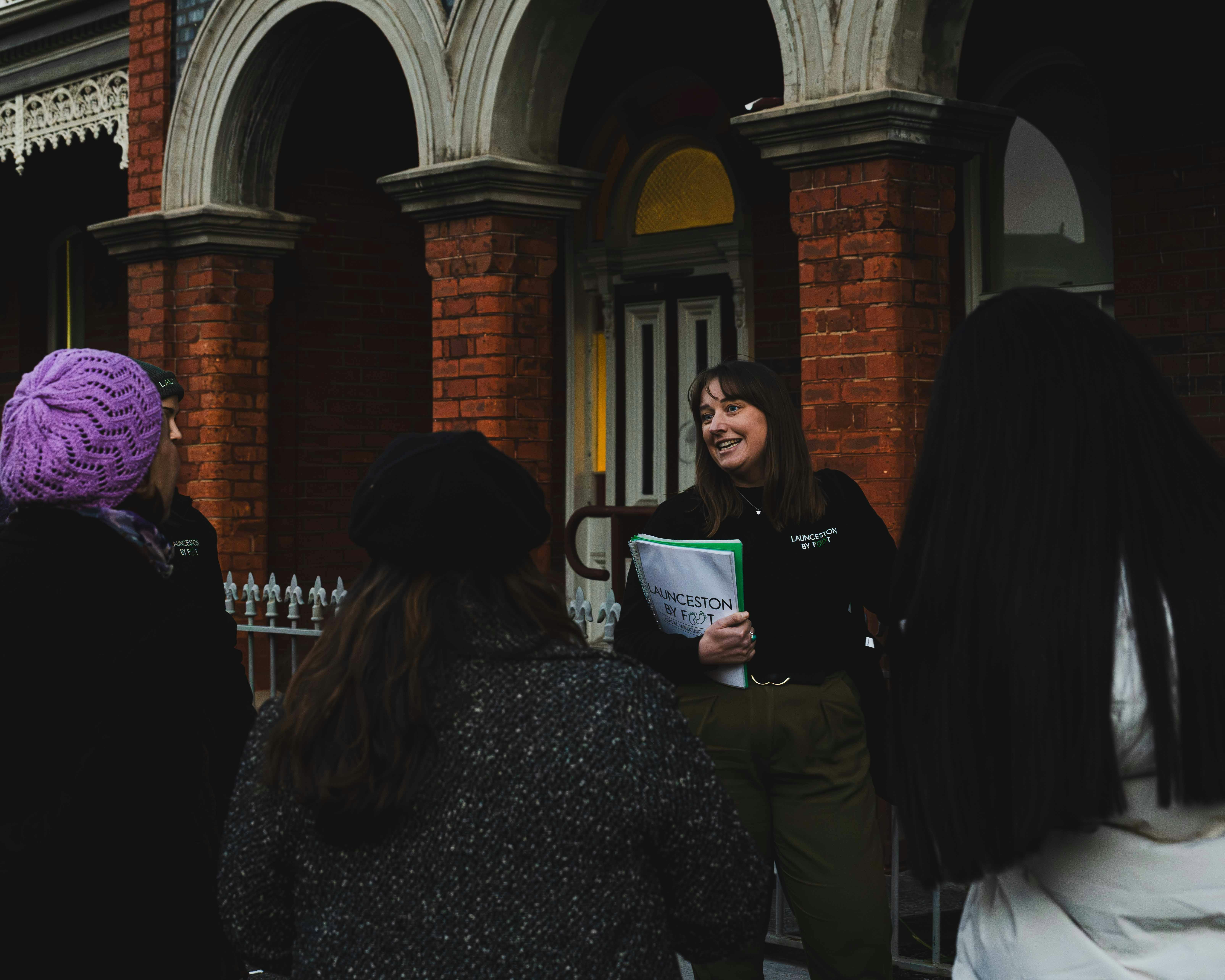 Launceston By Foot guide sharing a story with guests outside a historic red-brick building.