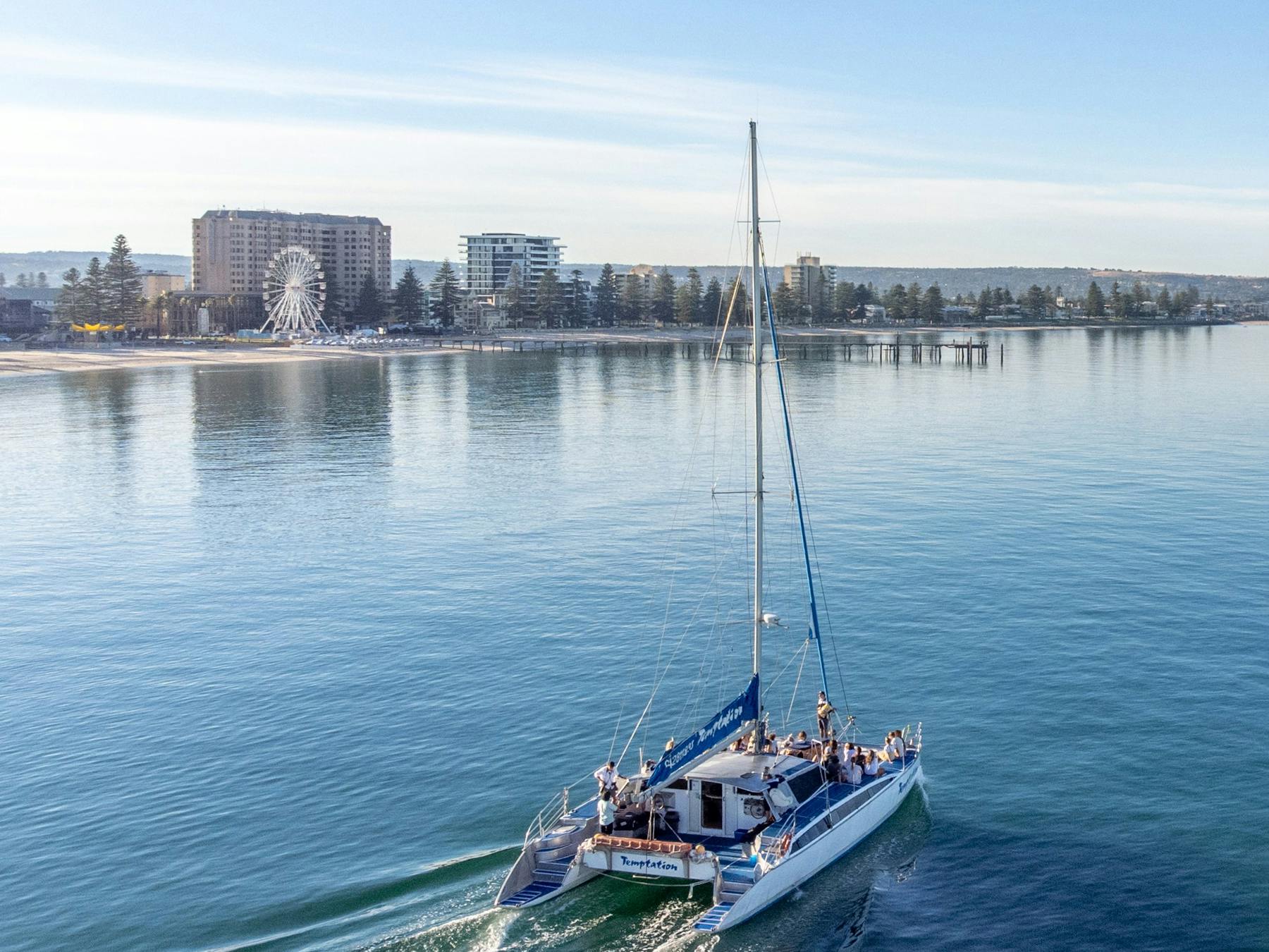 A catamaran cruising along the foreshore with passengers