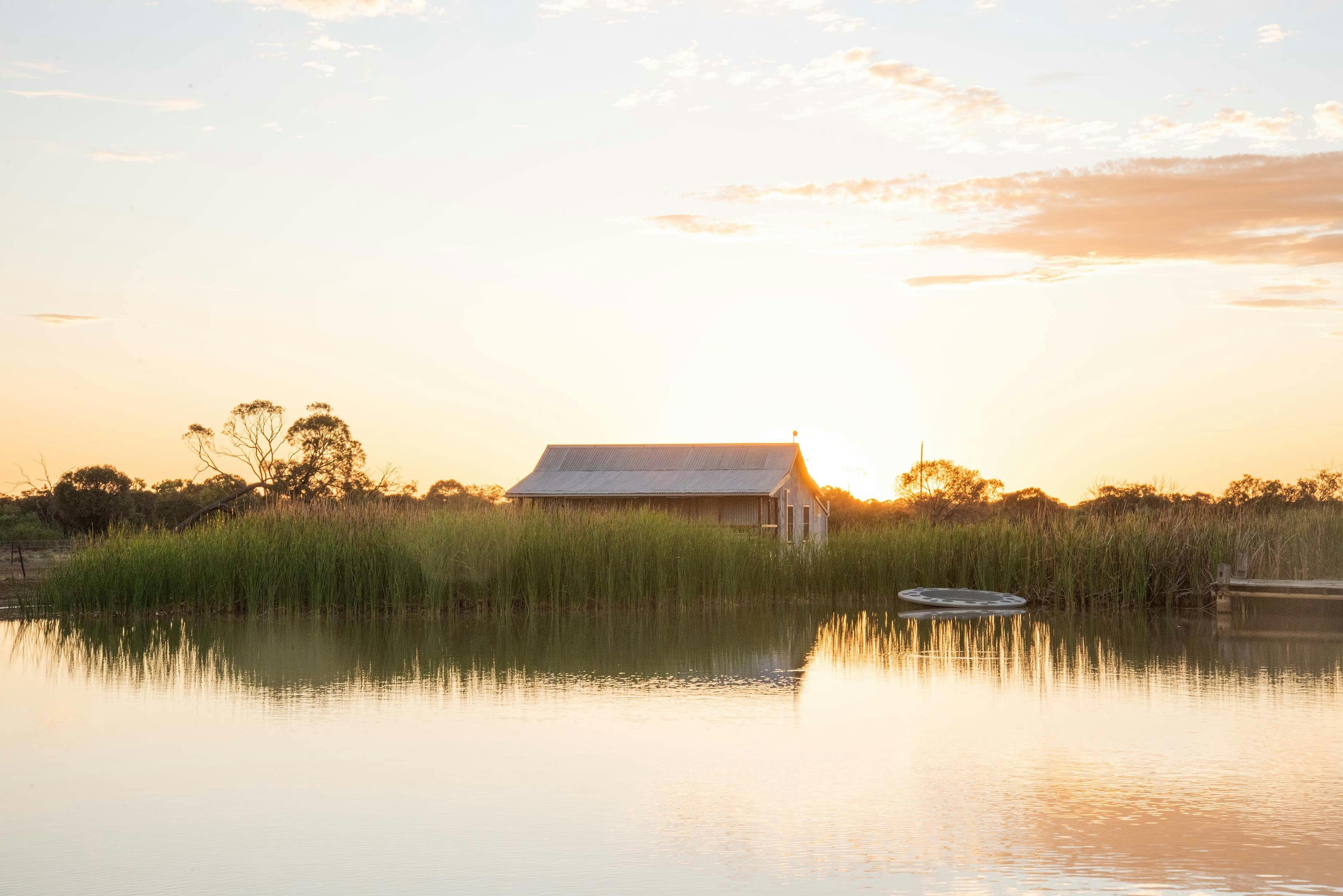 A view of a cottage adjacent to a lake at sunset