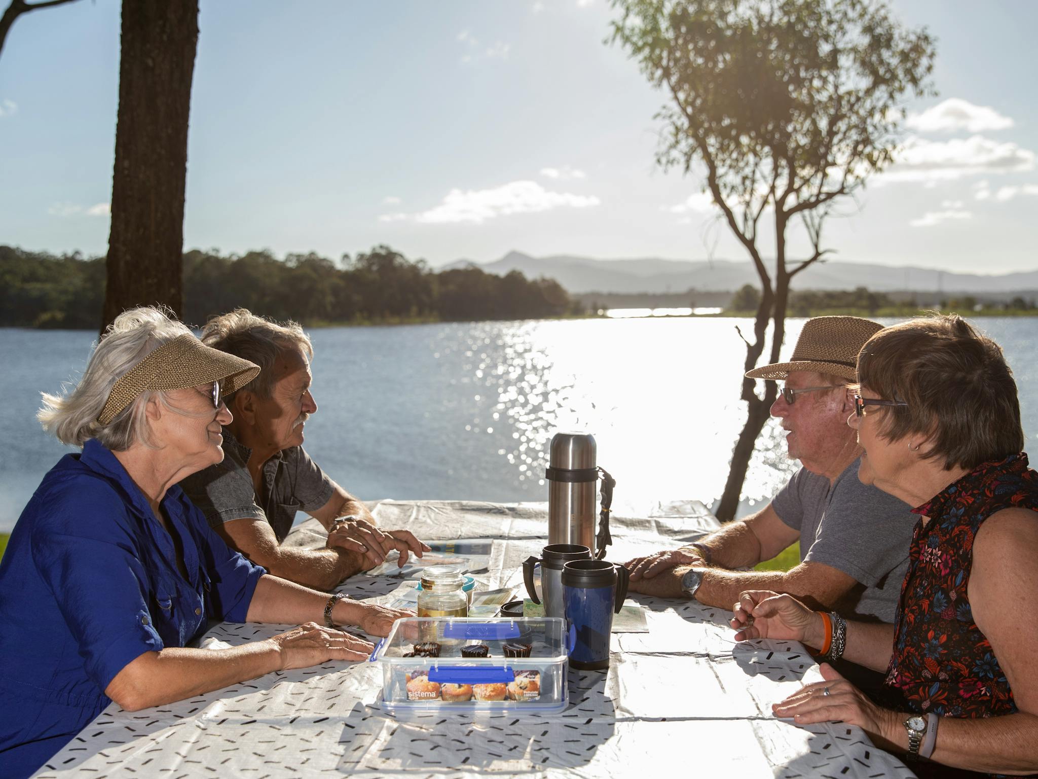 Two elderly couples sitting at a picnic table beside Lake Samsonvale eating and drinking tea Two elderly couples sitting at a picnic table beside Lake Samsonvale eating and drinking tea