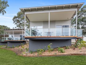 Villa with deck positioned above green grass and gardens