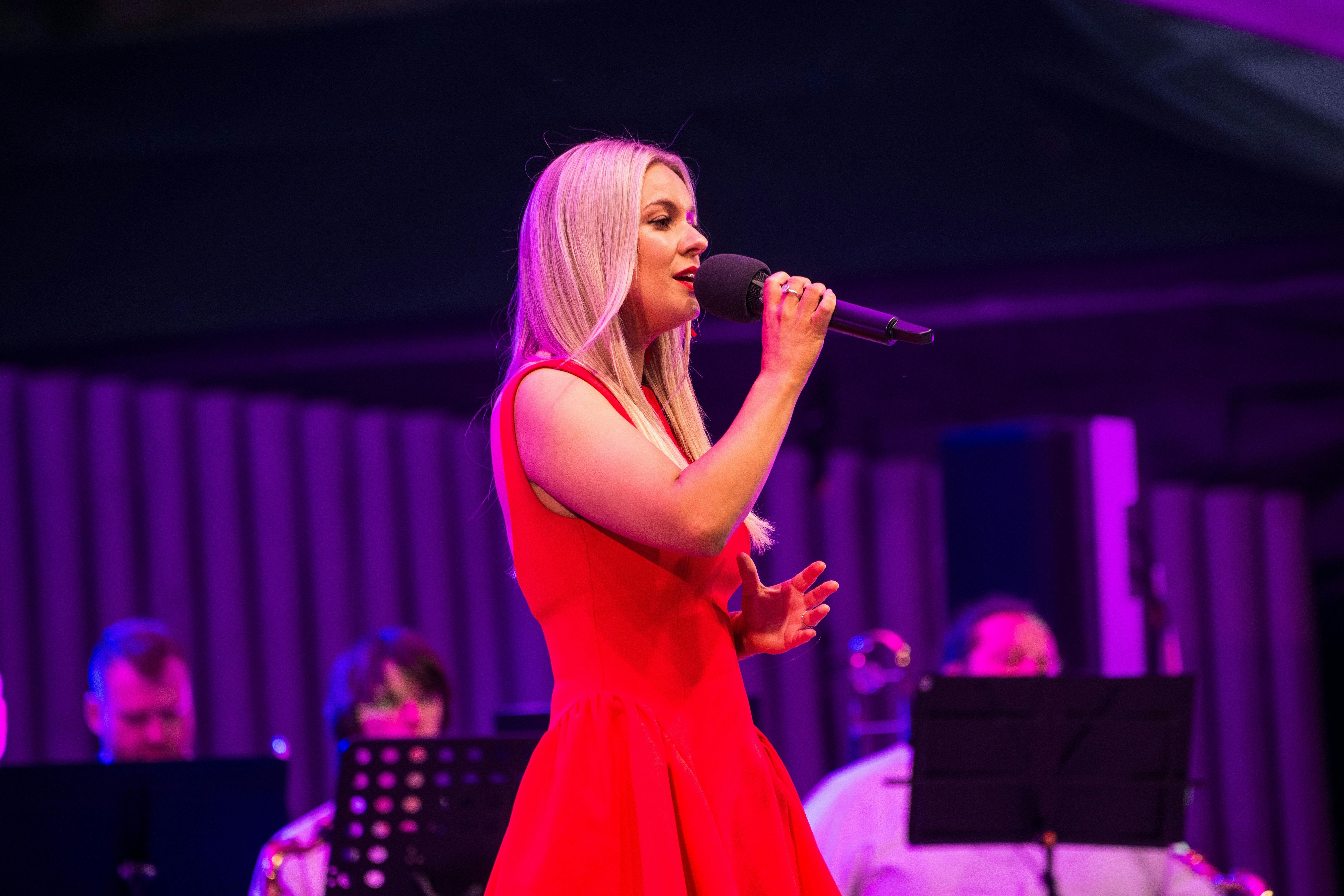 muscial artist with blond hair and red dress singing Christmas Carols