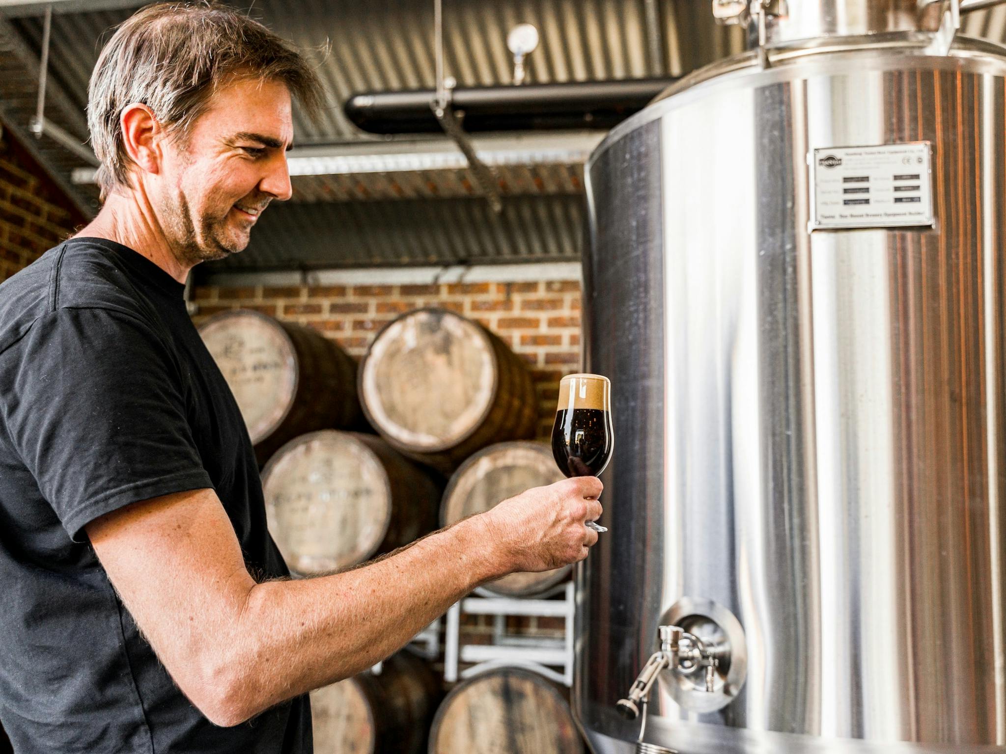 The head brewer stands in front of fermenters with a stout
