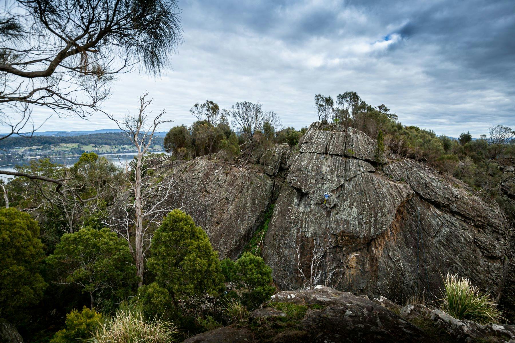 Sheer rock faces against a backdrop of moody clouds and bushland