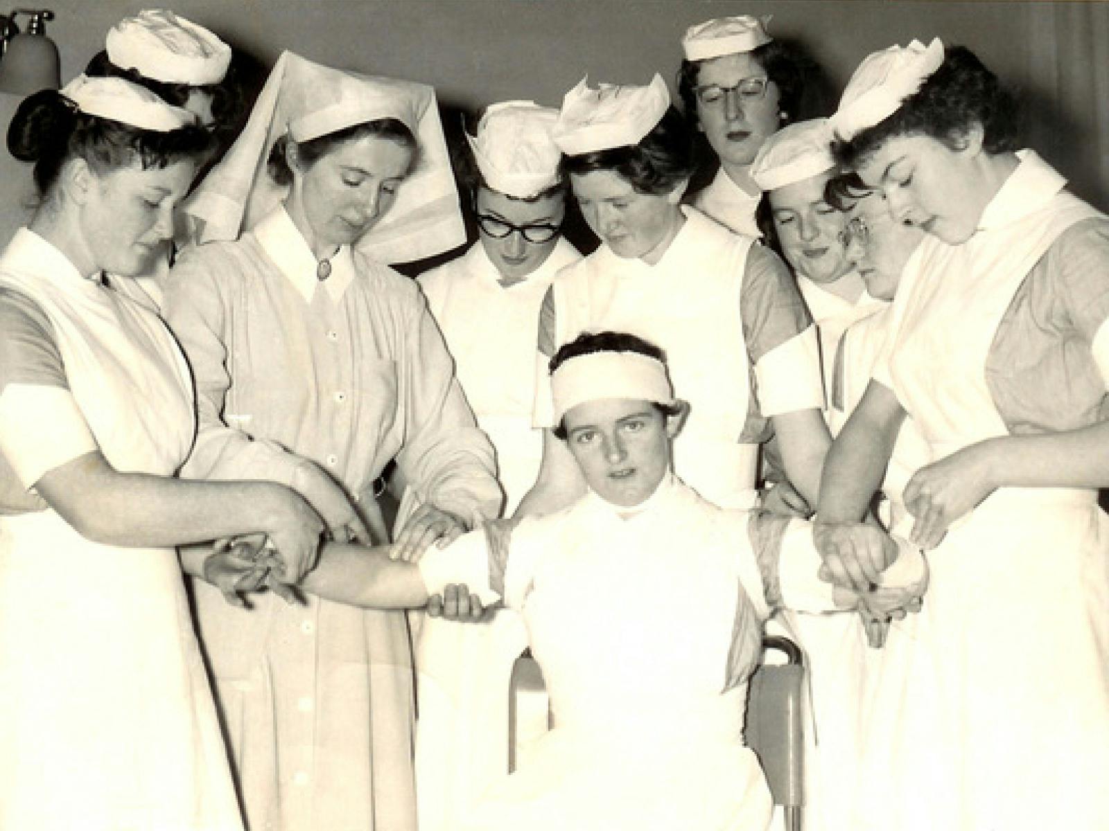 Black and white photo of nurses practicing bandages on one another - July 1958