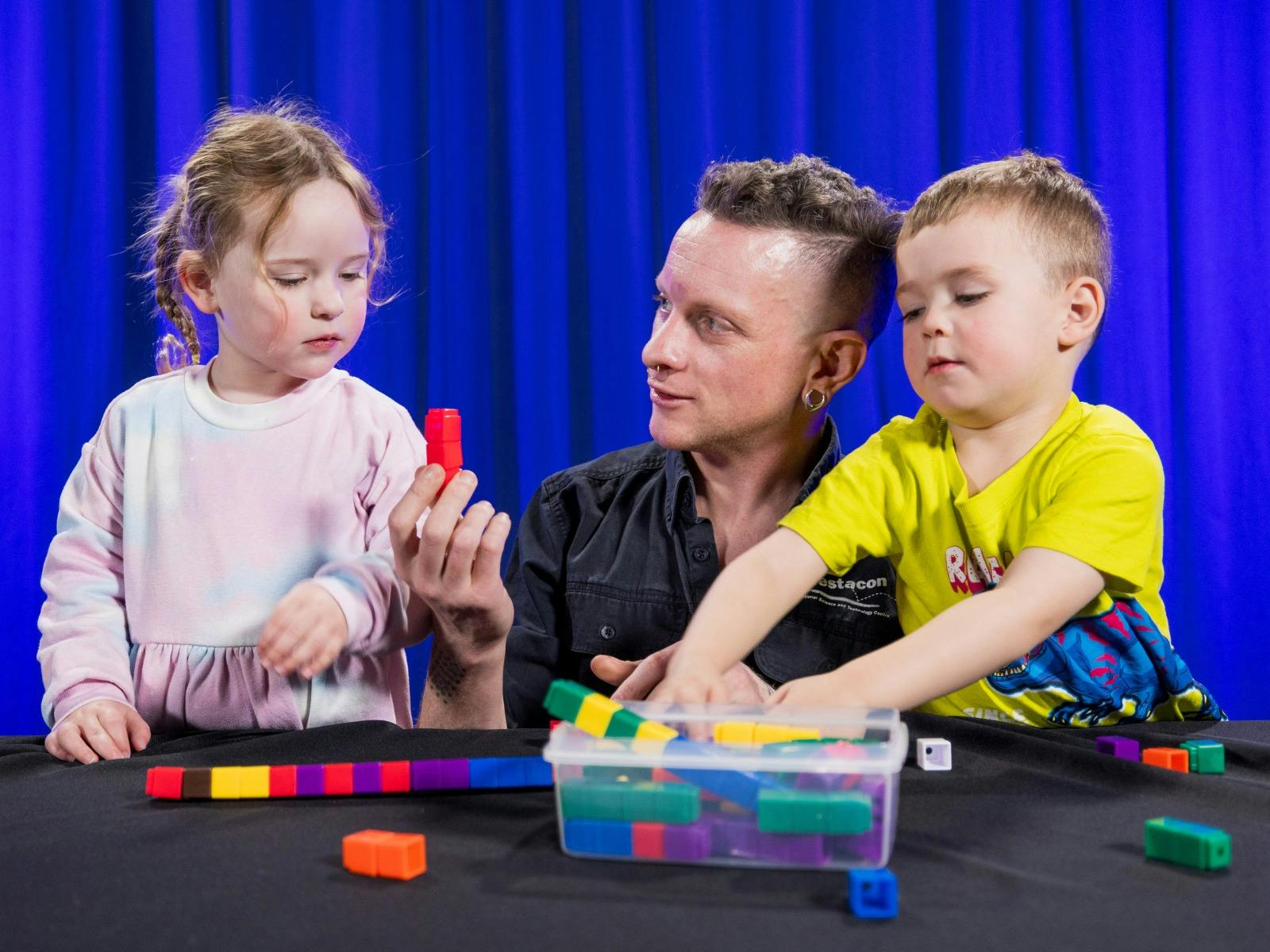 Two children and a man explore patterns using coloured blocks