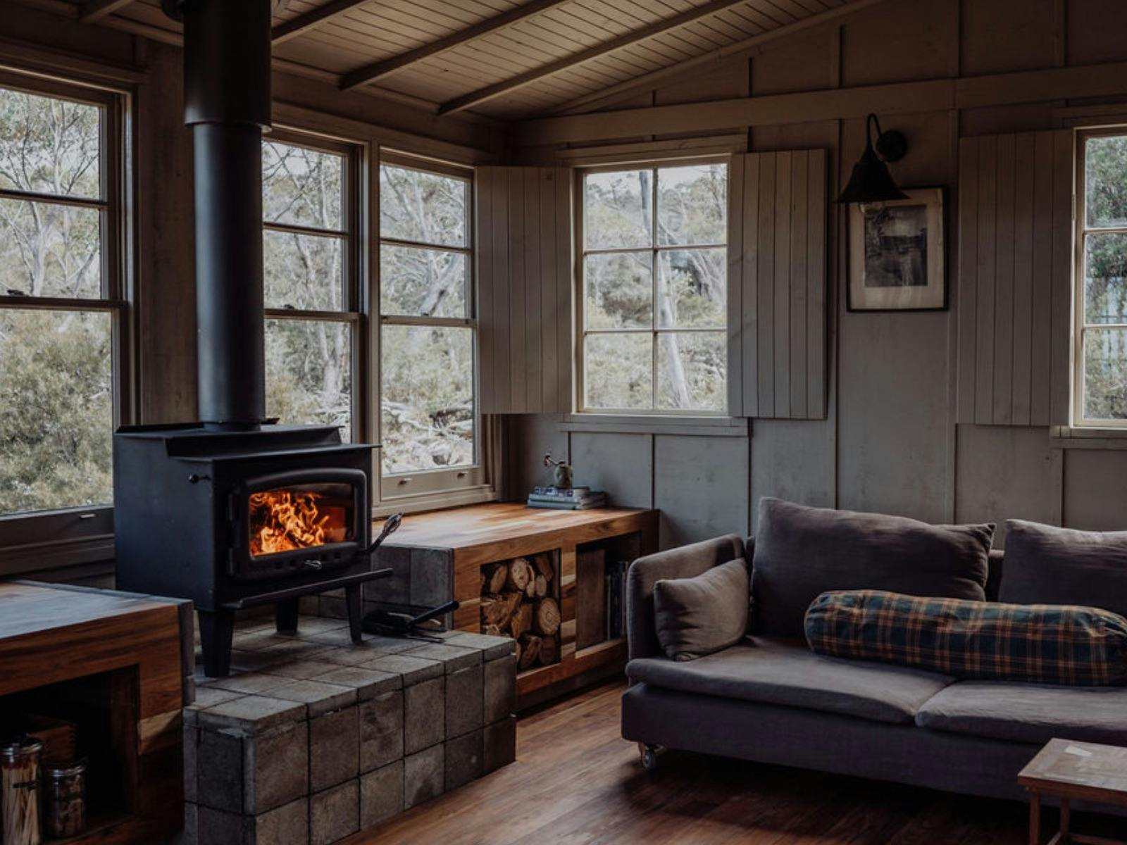 Camp living room with wood fireplace, large windows and lounge.