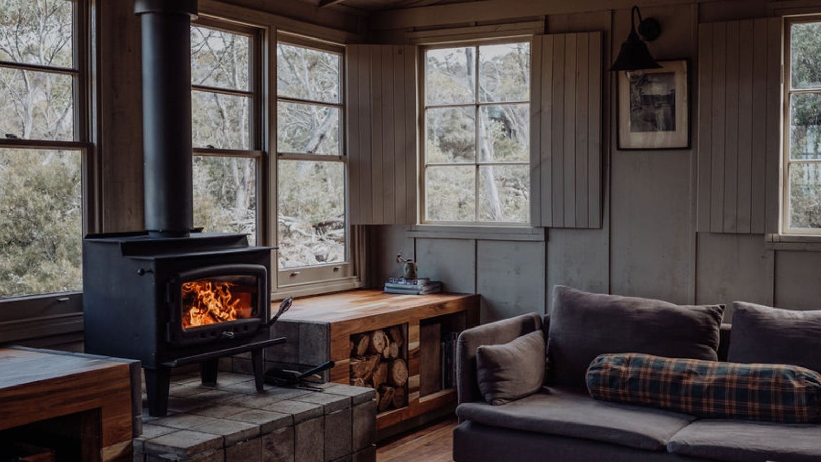 Camp living room with wood fireplace, large windows and lounge.