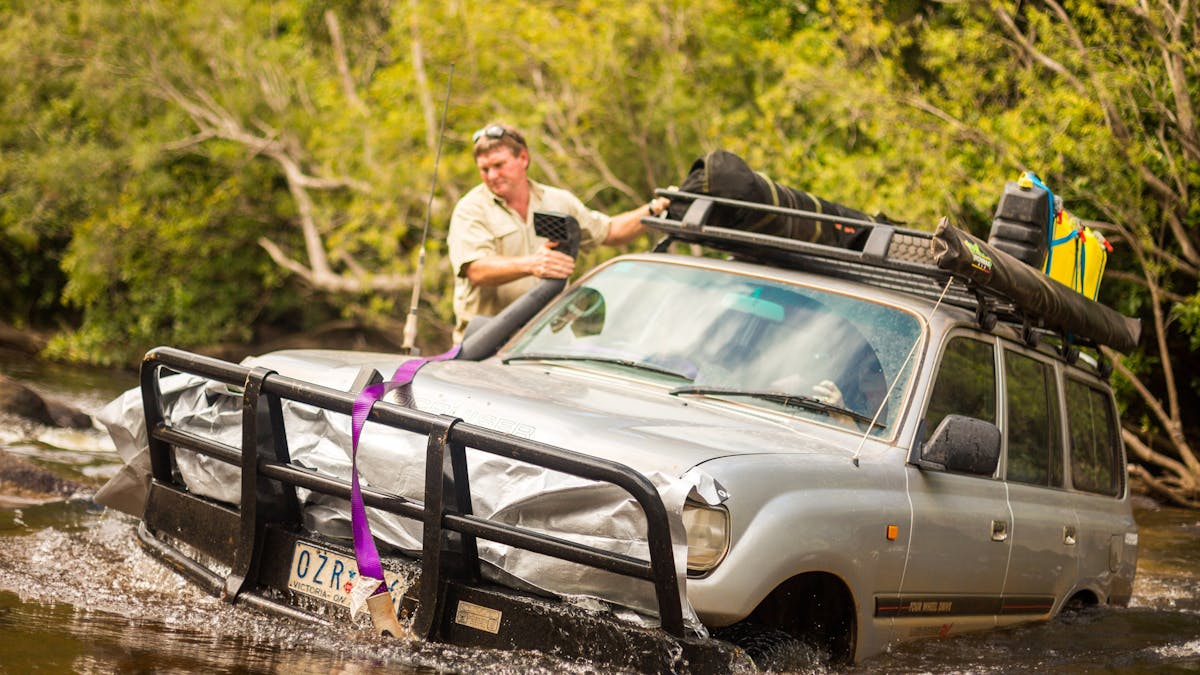 Toyota Landcruiser driving through deep water crossing with guide stood on side step ready to help!
