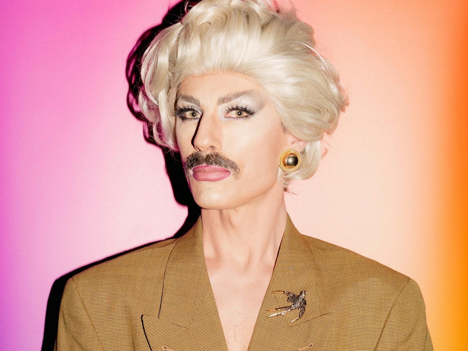 Drag artist man wearing a blonde wig and brown moustache