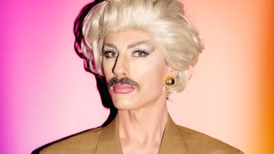 Drag artist man wearing a blonde wig and brown moustache
