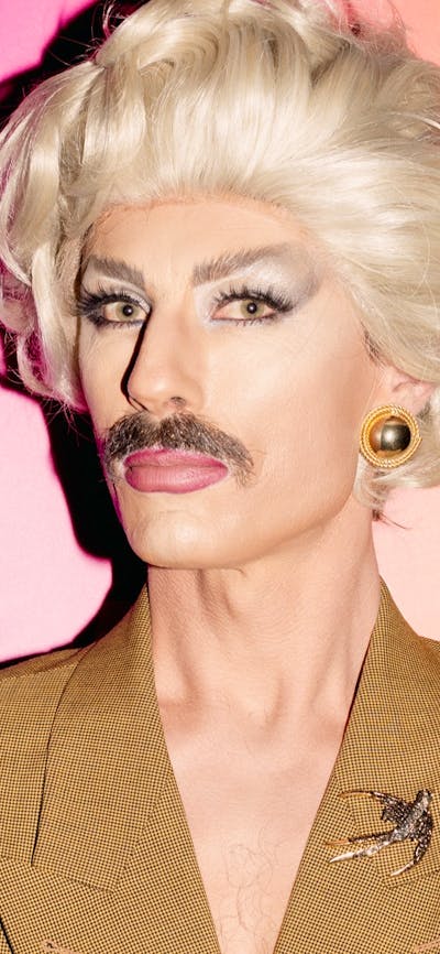 Drag artist man wearing a blonde wig and brown moustache