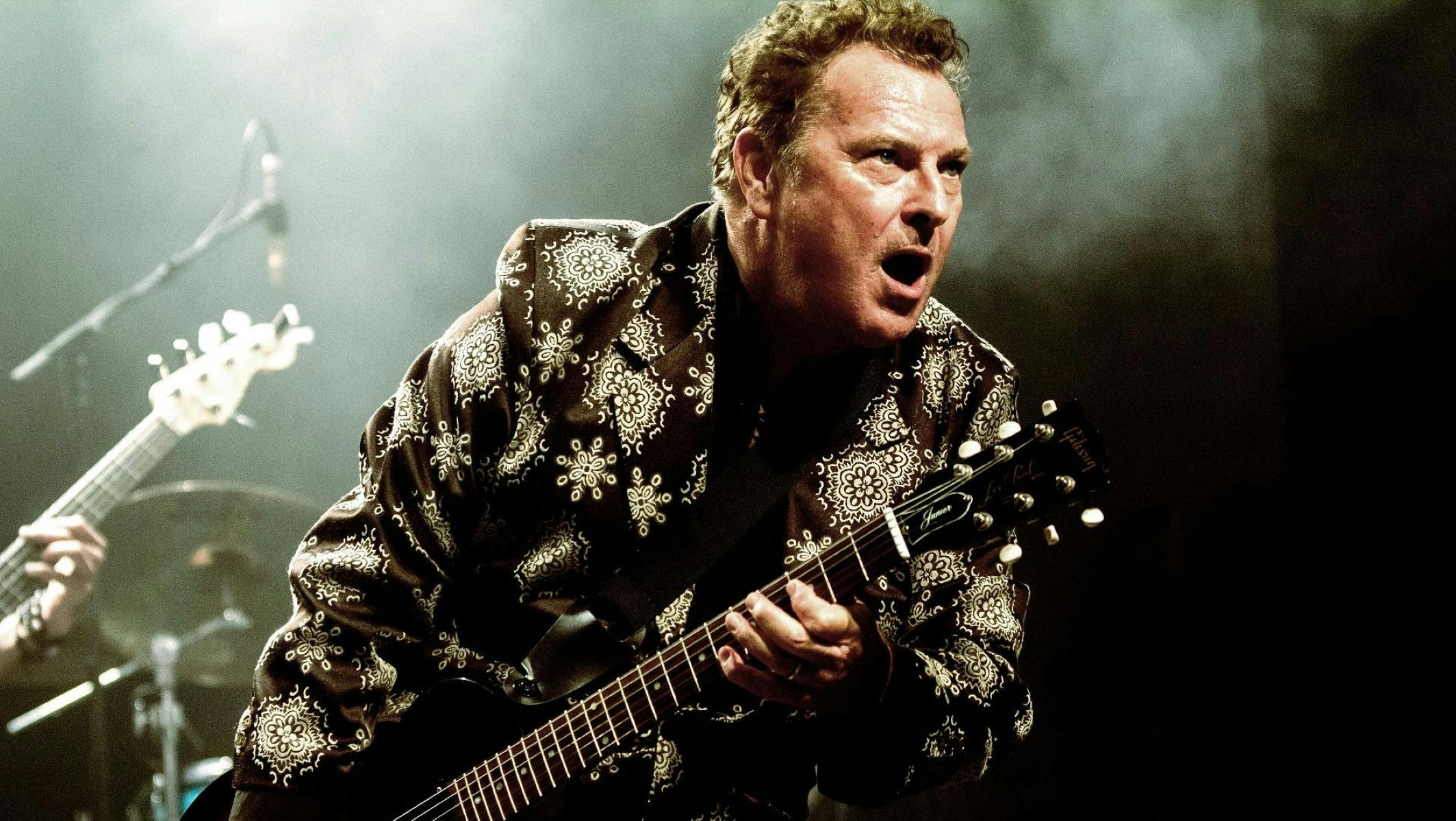 An Image of a man leaning forward singing and playing the guitar