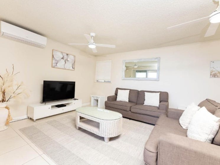 Air-conditioned lounge room with TV, lounges and coastal decor