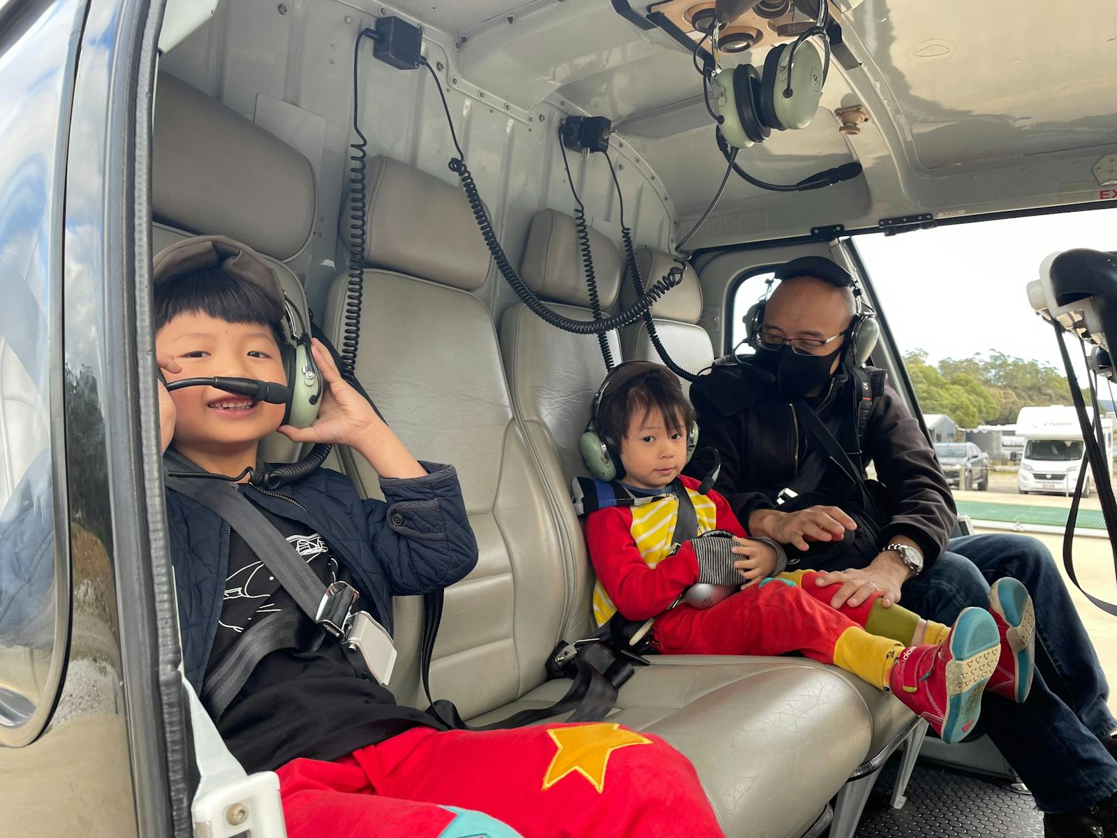 Two young children with their father smiling at the camera, with headsets on and ready to fly.