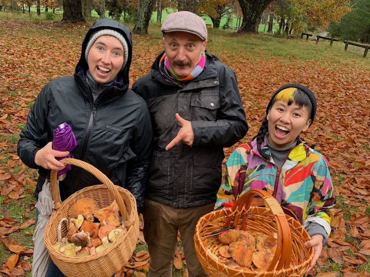 Three people with big smiles and two basket full of mushrooms