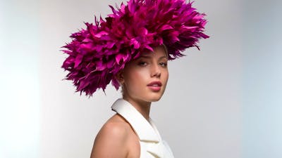 The photograph depicts a model wearing a unique pink headwear piece similar to a flower blooming.