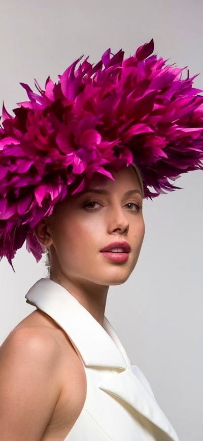 The photograph depicts a model wearing a unique pink headwear piece similar to a flower blooming.