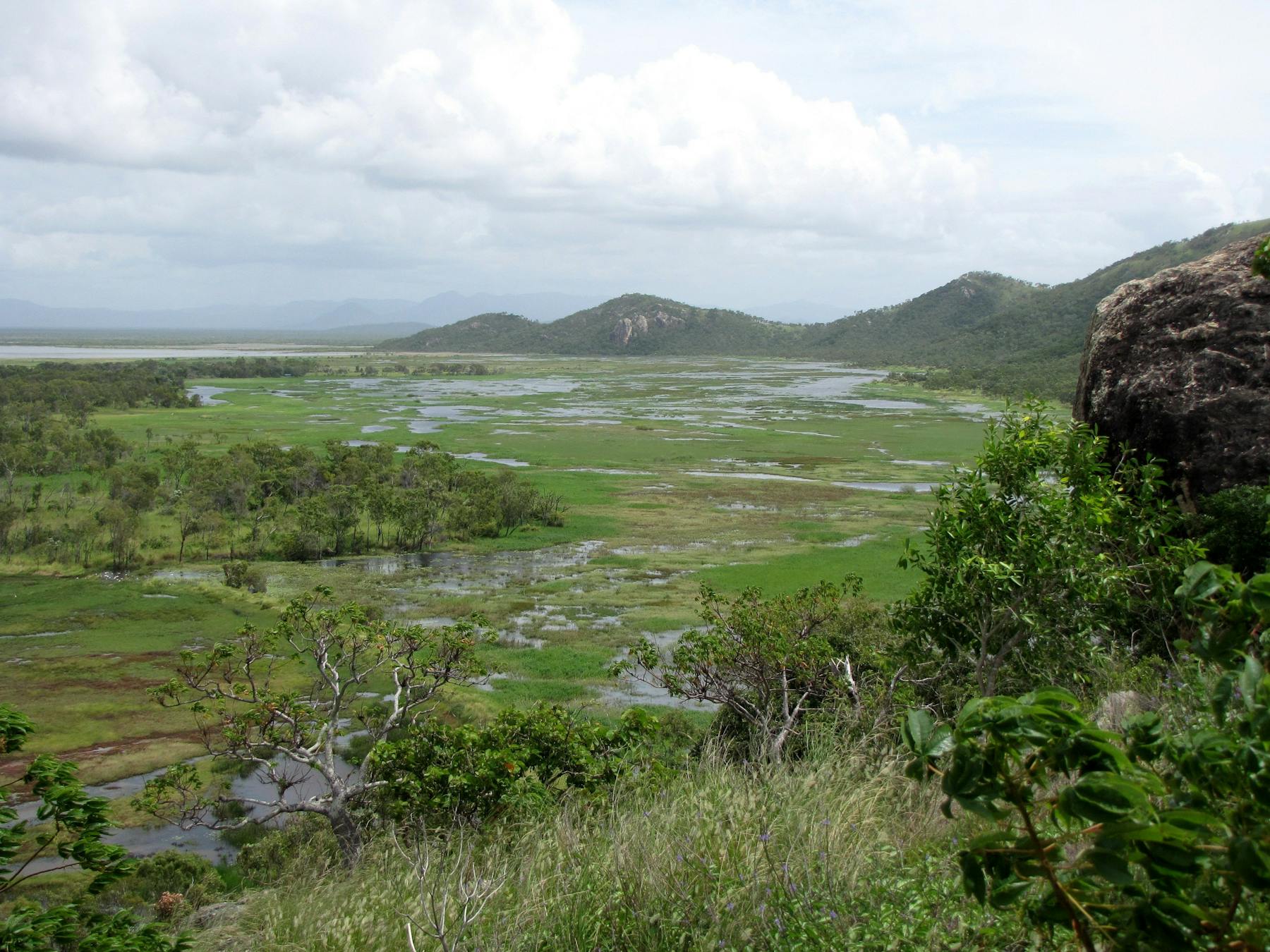 Views of coastal plain, distant mountains and ocean from high vantage point.