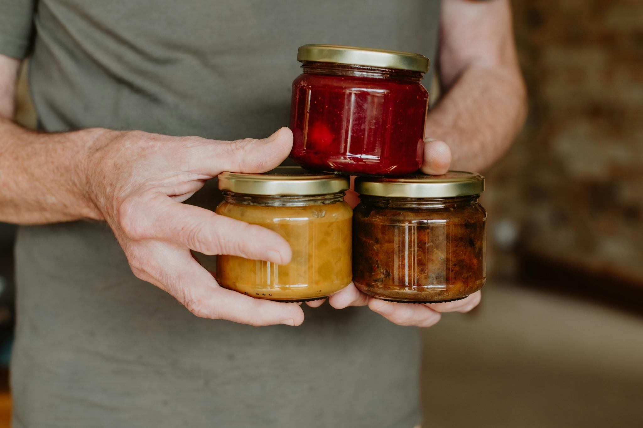 Cooks hands holding jars of homemade produce, including  strawberry jam, chutney and relish