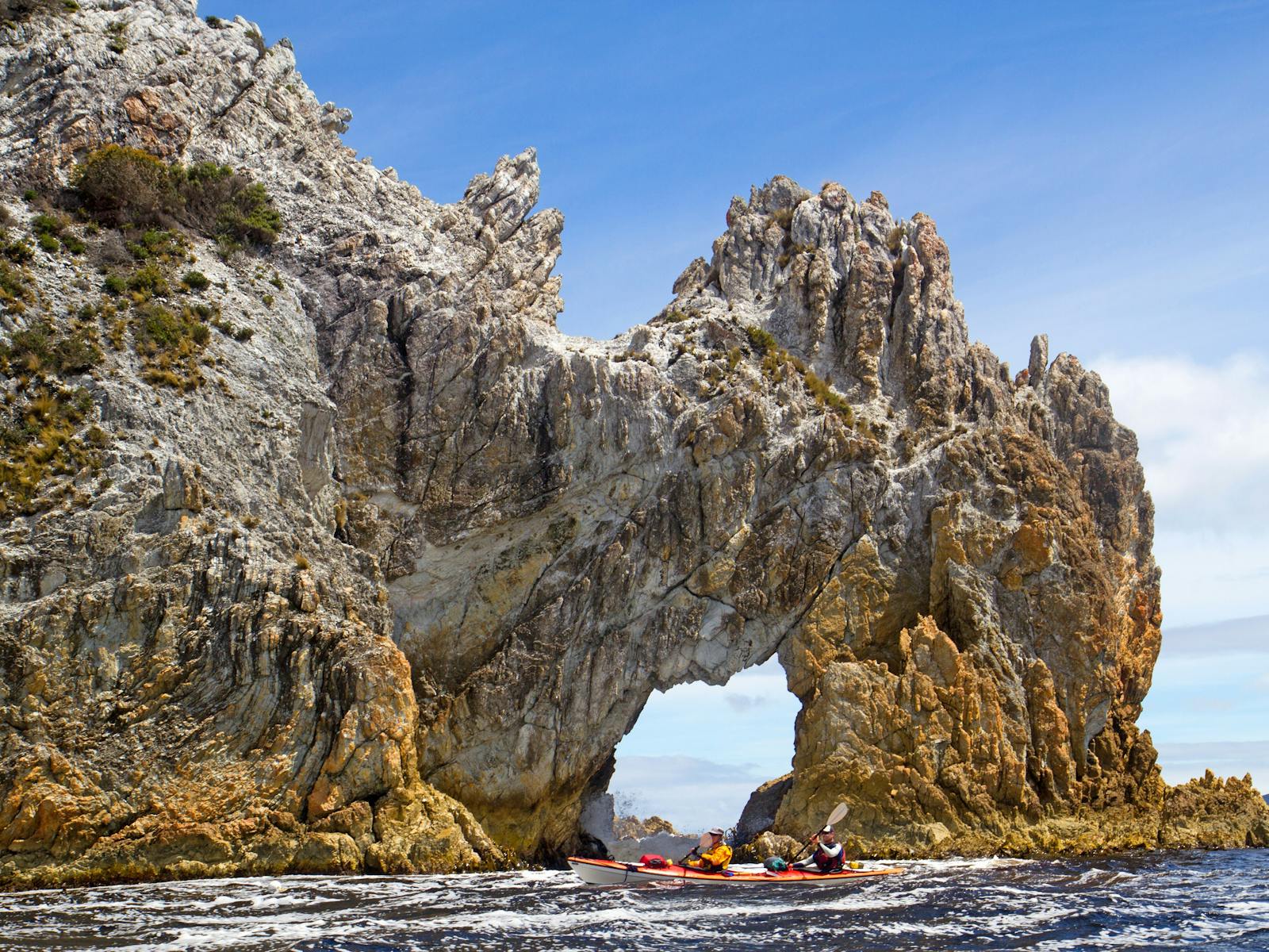 Kayakers paddling beside Wallaby Arch on Port Davey