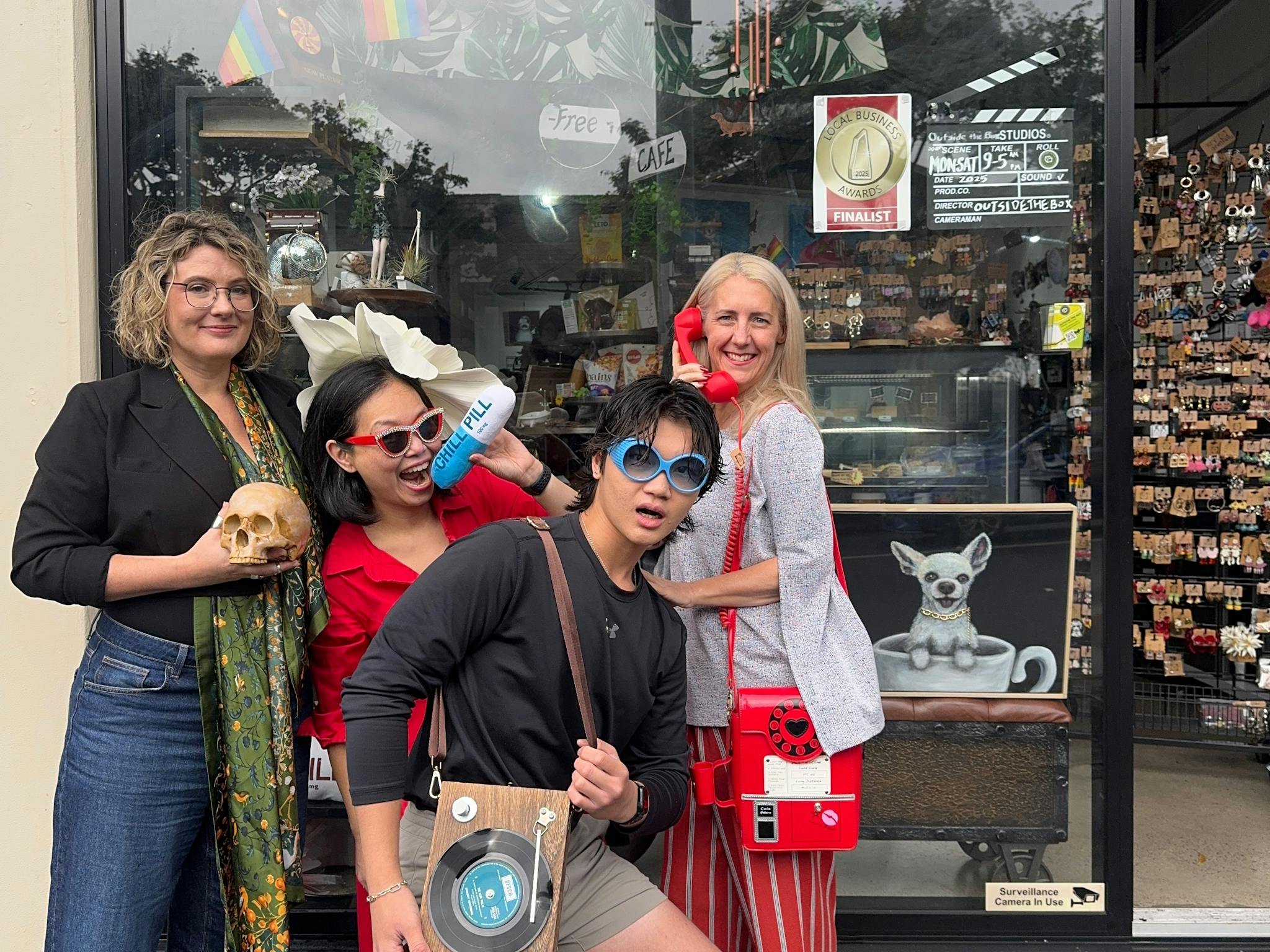 Staff posing outside the store with fun handbags, a skull, oversized flower hat & Chill Pill pillow Staff posing outside the store with fun handbags, a skull, oversized flower hat & Chill Pill pillow
