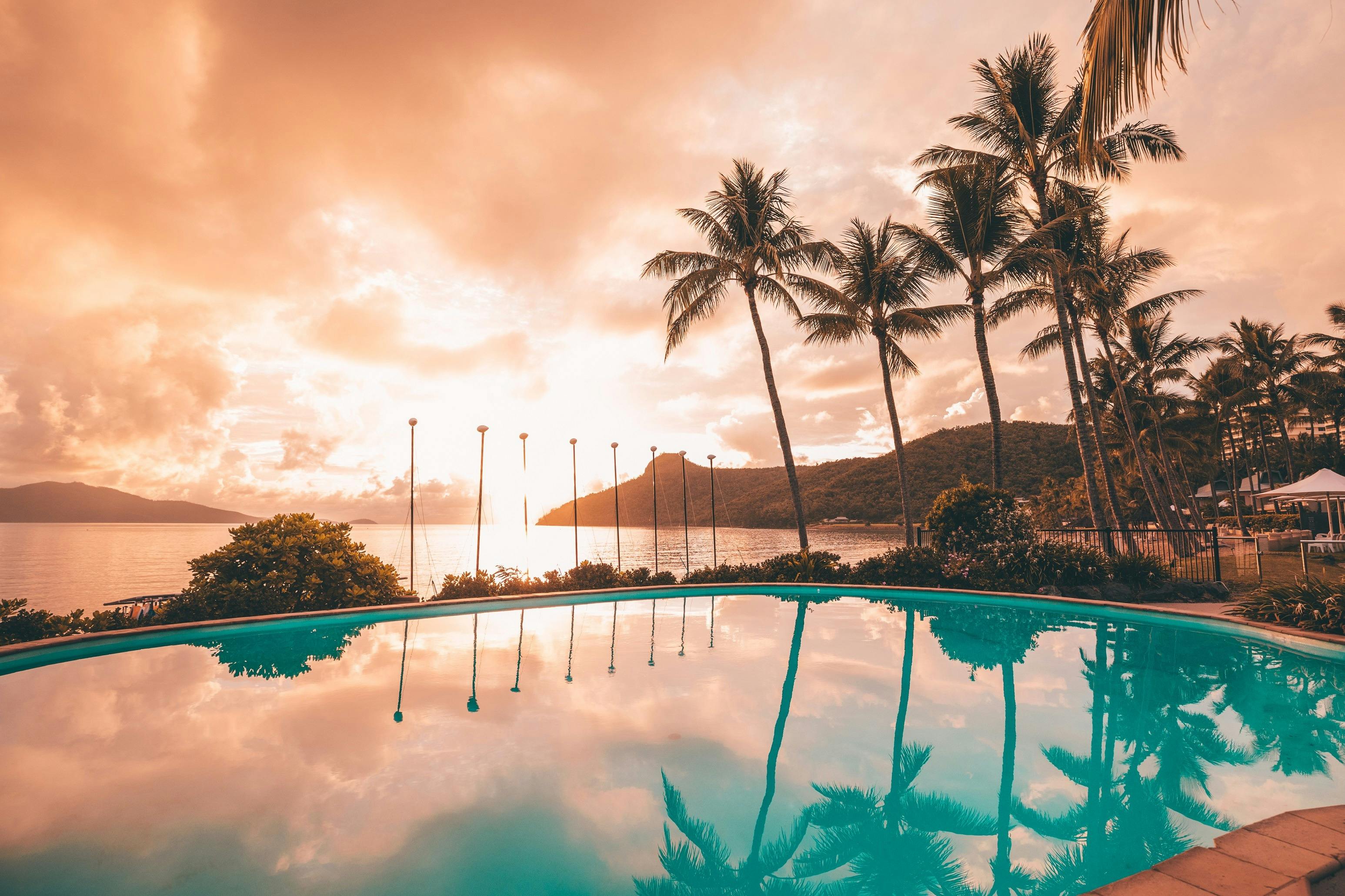 Stunning pink sunset views from a pool with palm trees and islands in the backrgound