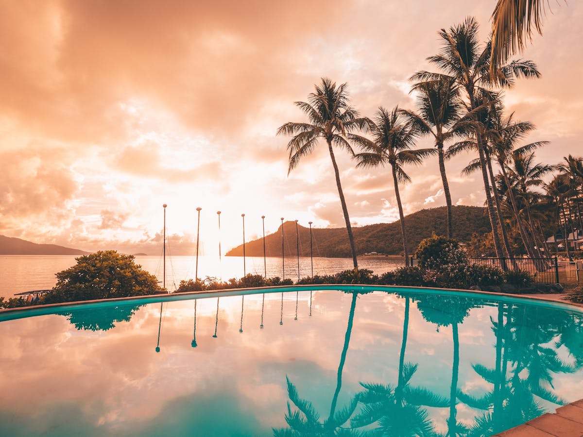Stunning pink sunset views from a pool with palm trees and islands in the backrgound