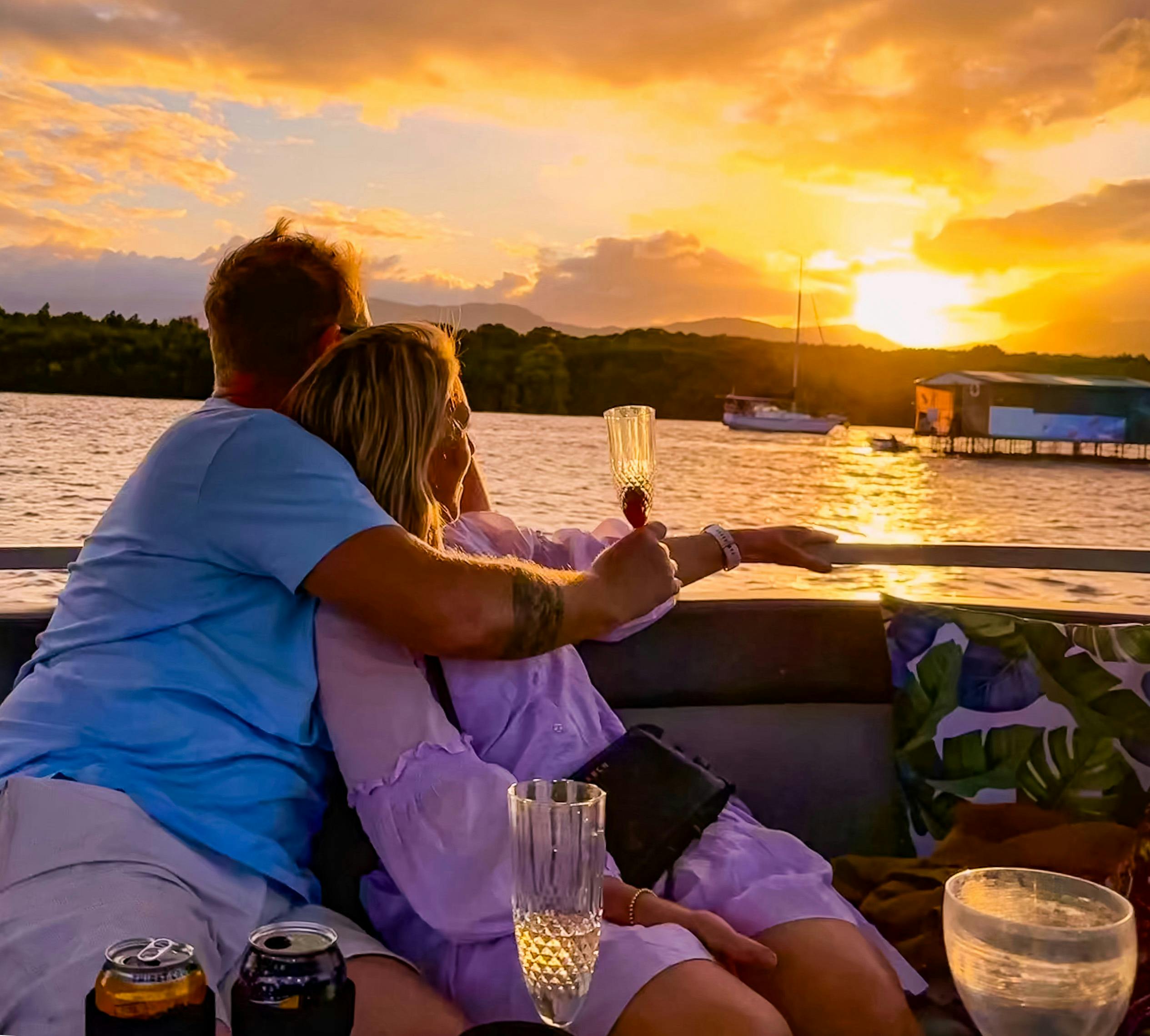 A couple embraced holding drinks and watching the sunset on the Cairns River Cruise