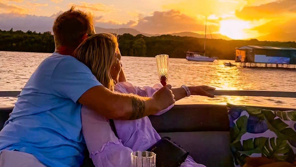 A couple embraced holding drinks and watching the sunset on the Cairns River Cruise