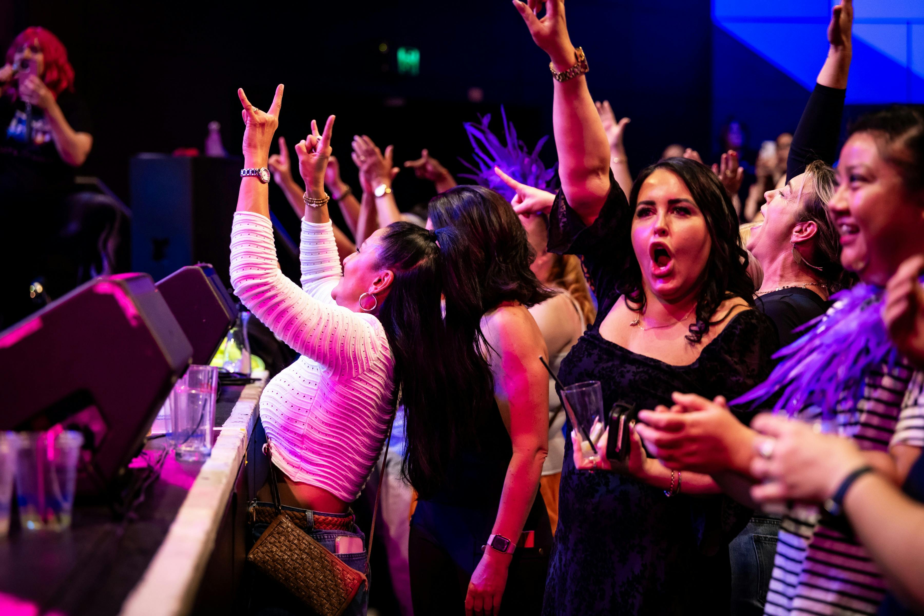 A crowd of ladies dance with hands in the air in front of the stage