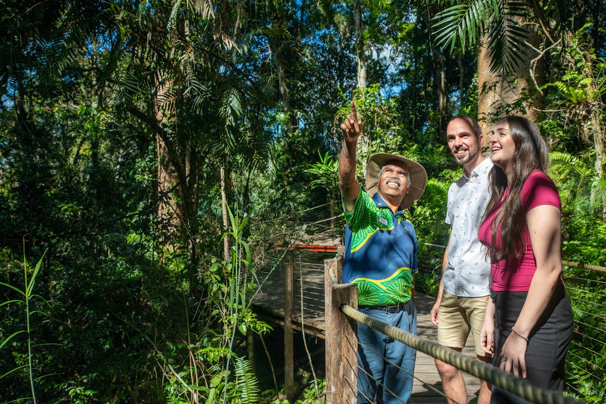 Lady and man standing in the rainforest next to a Ranger Guide pointing up