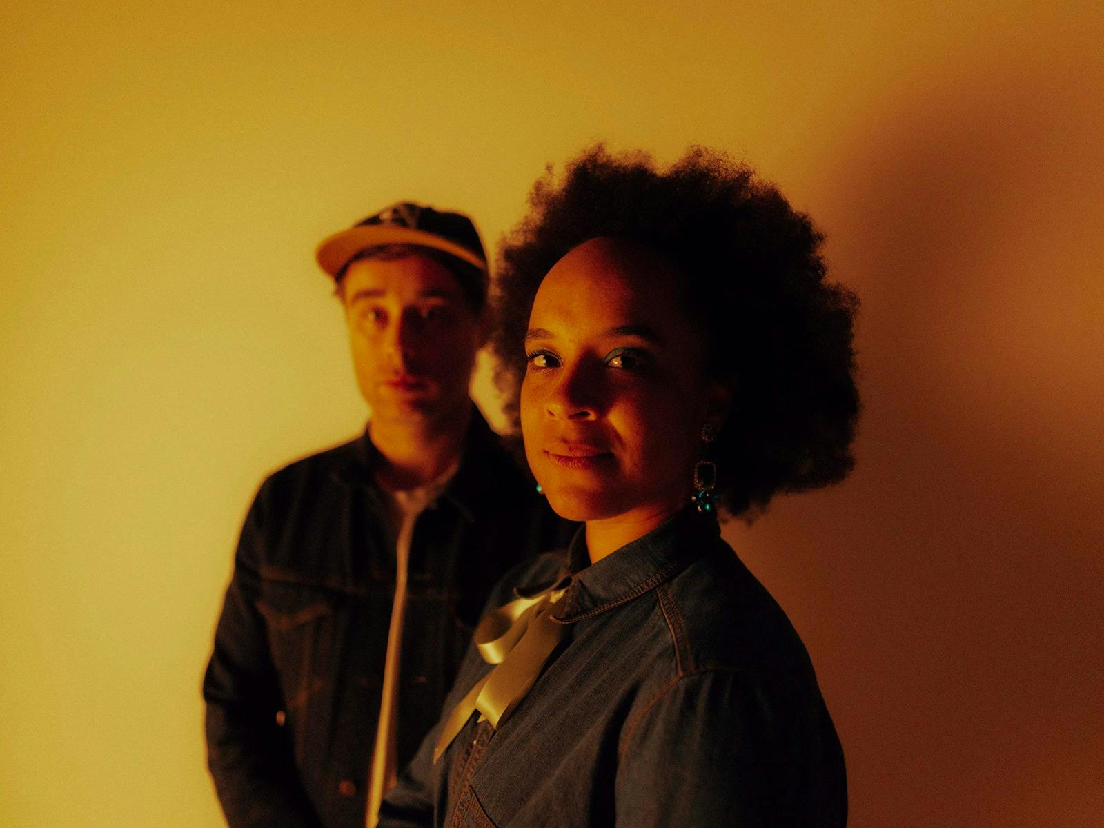 Two artists in low lighting against a yellow backdrop
