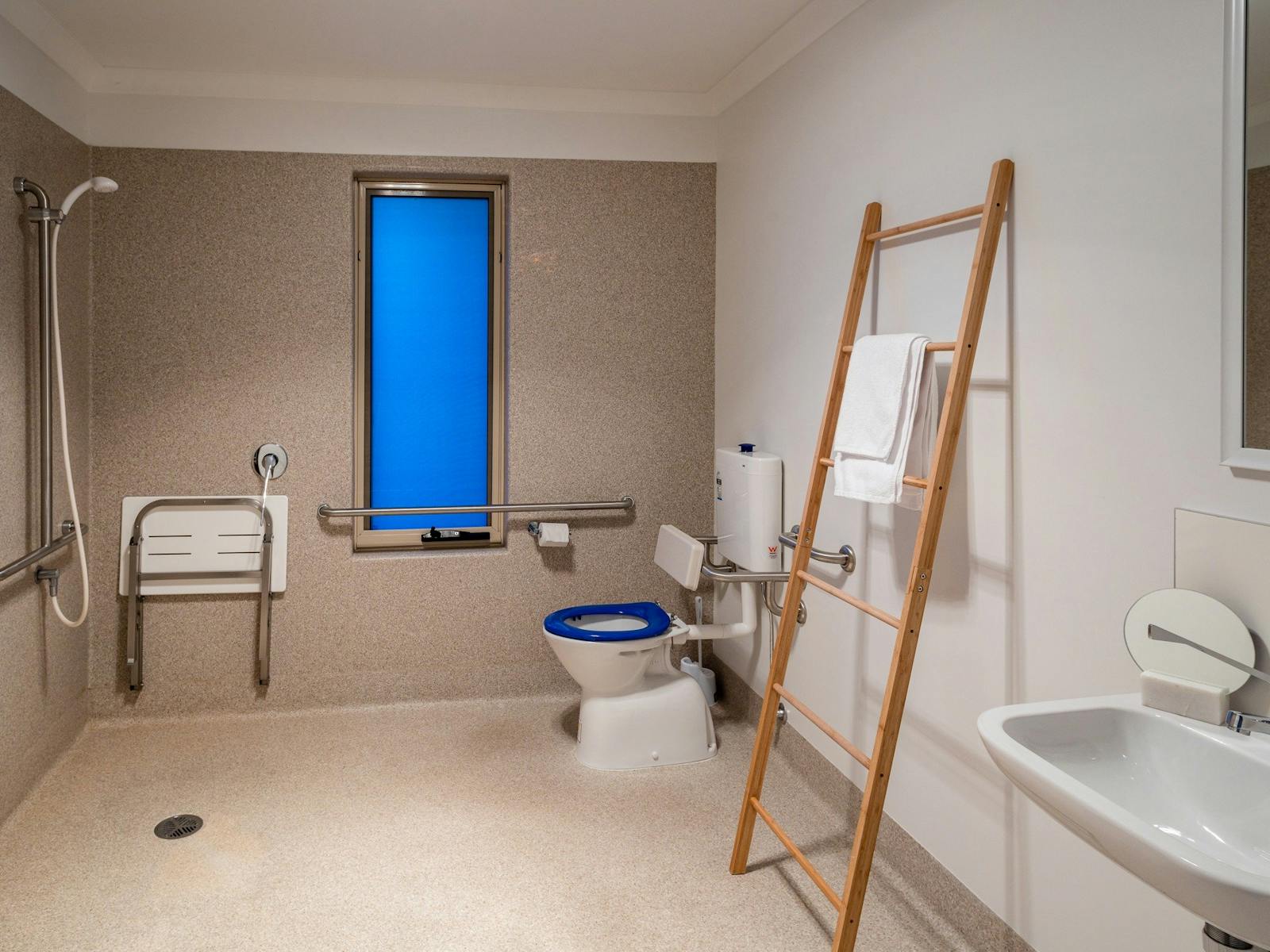 The main bathroom has an open shower space with grab rails and seat, toilet with grab rails basin..