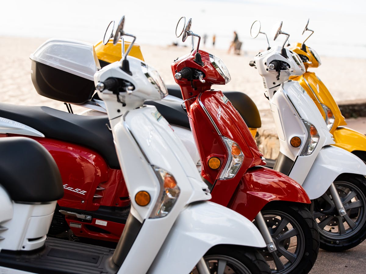 Close up photo of 4 different coloured scooters lined up with beach in background in Noosa