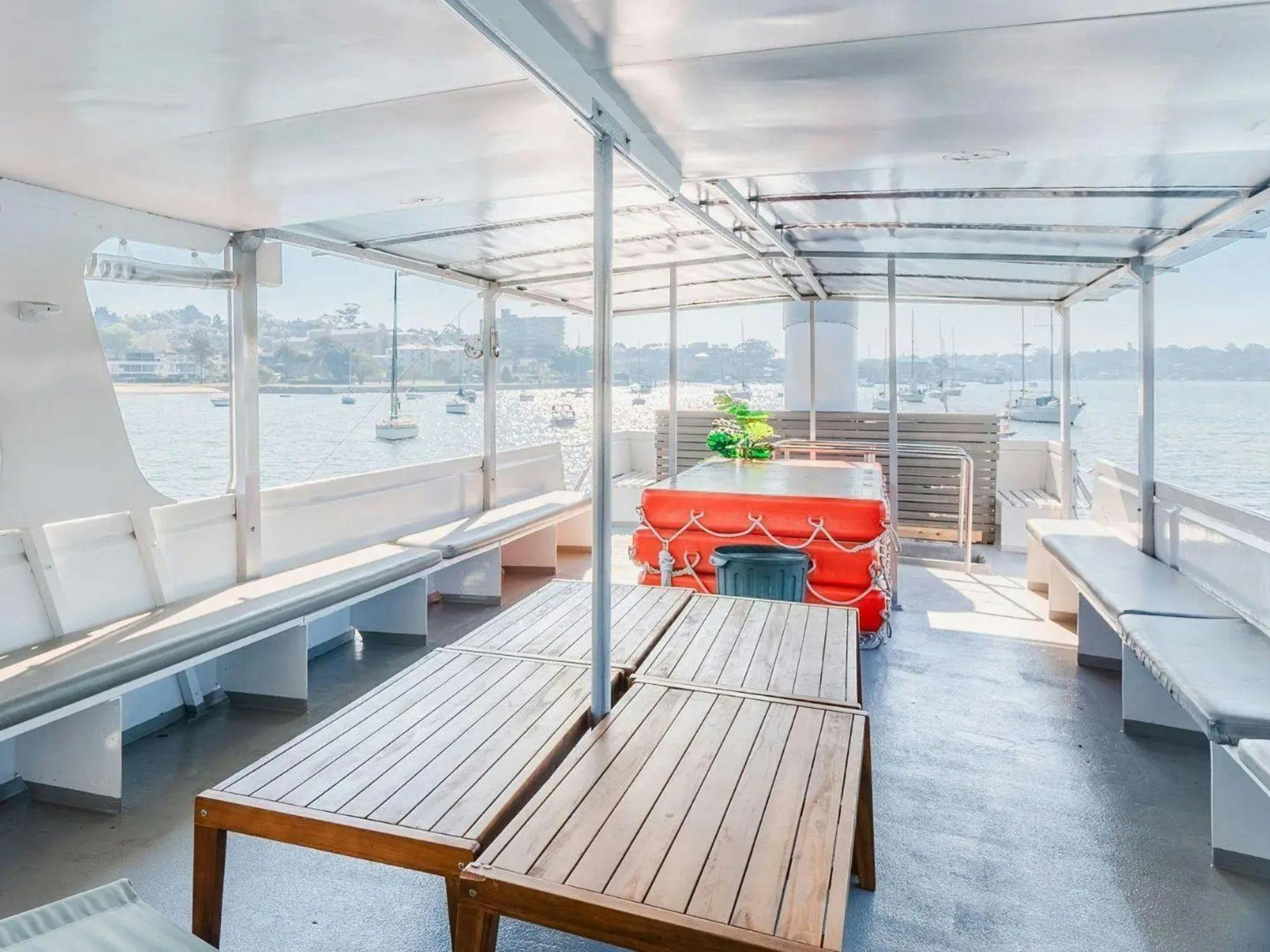 Covered upper deck of Zahara with bench seating and a table, overlooking the harbour