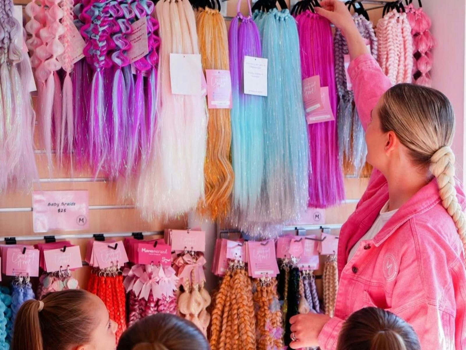Coloured hair manes hanging on a wall with a lady in a pink shirt