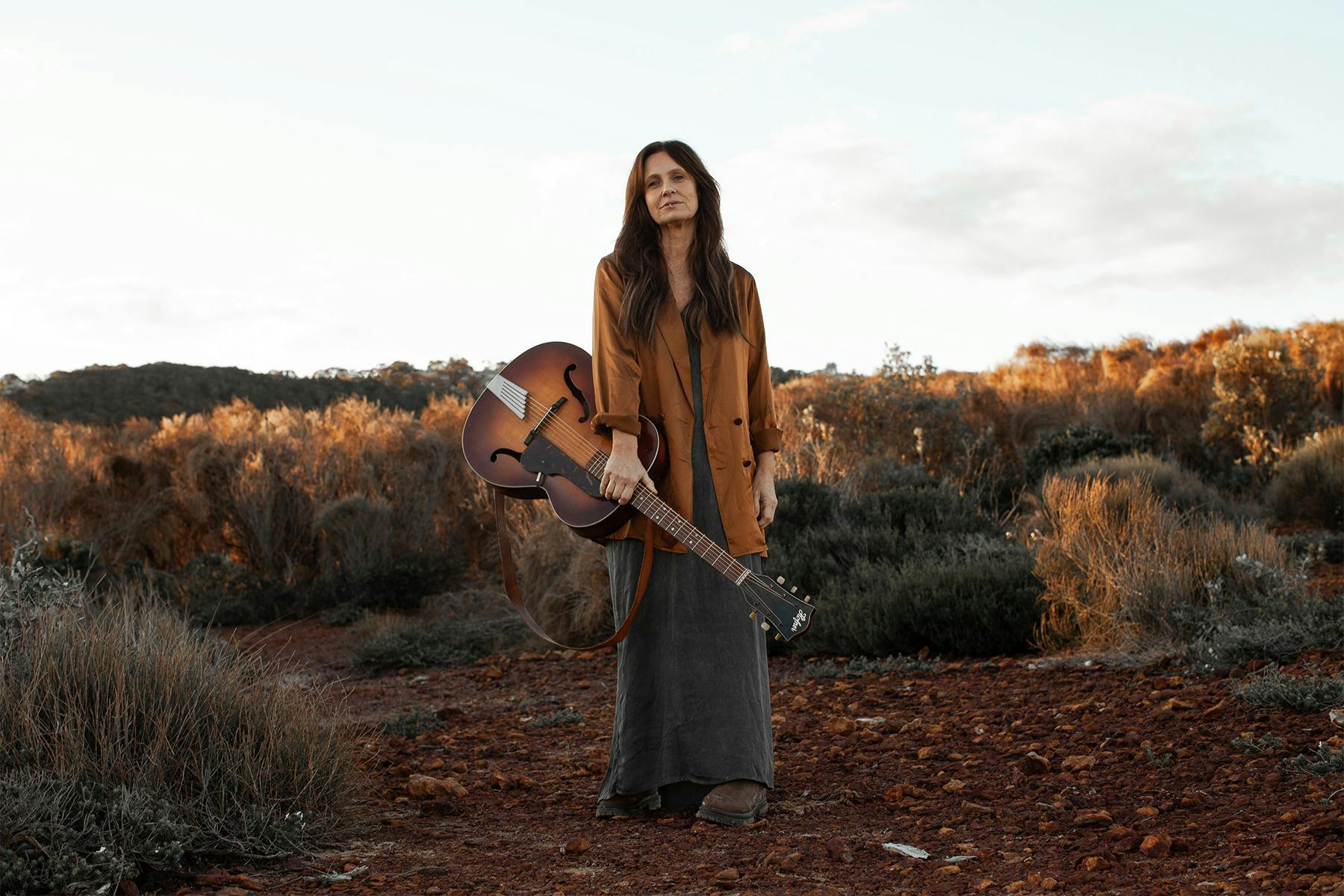 Kasey Chambers holding a guitar in a field.