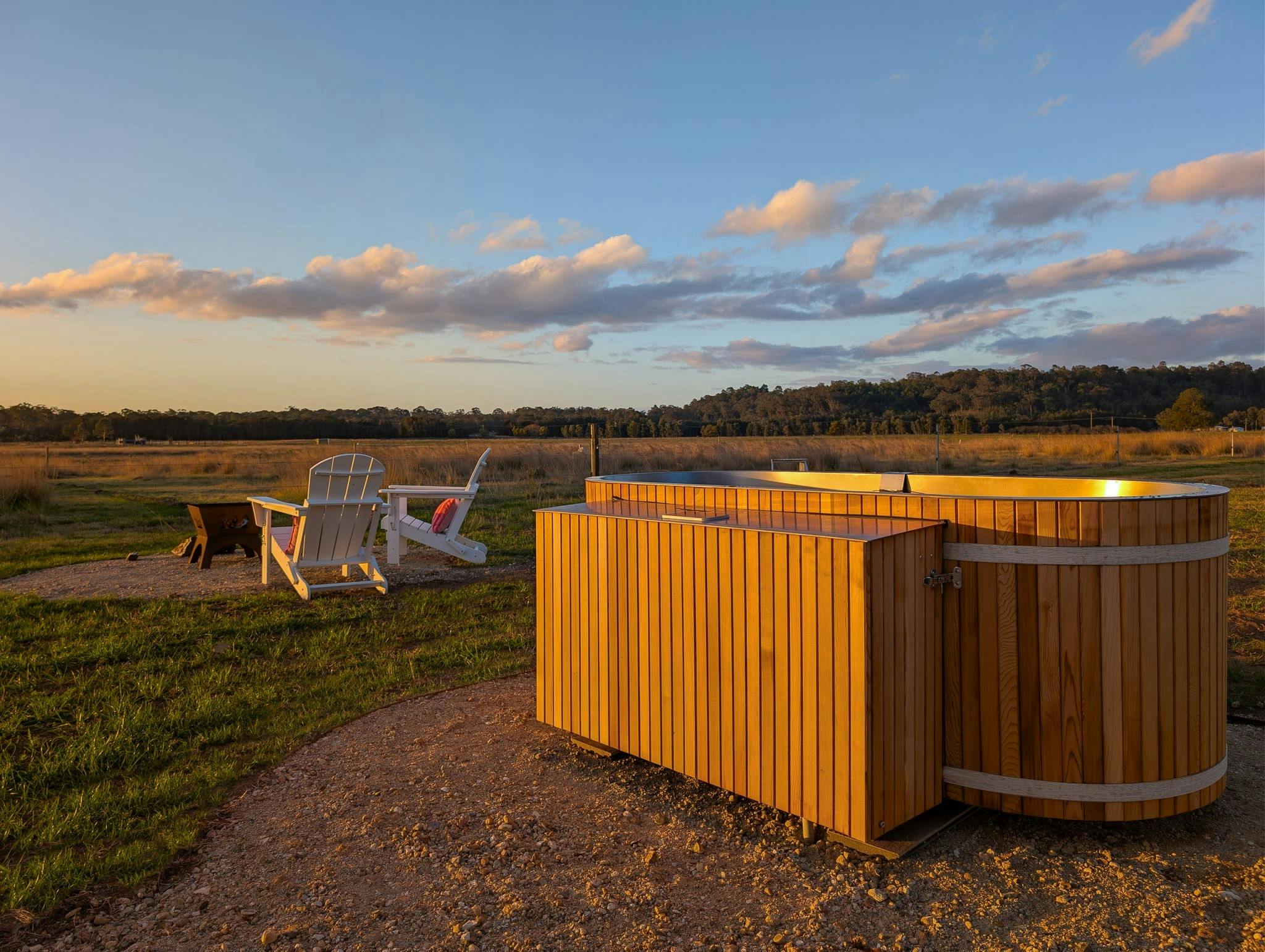 The Caravan's outdoor bath for two in the paddock at golden hour, firepit chairs behind
