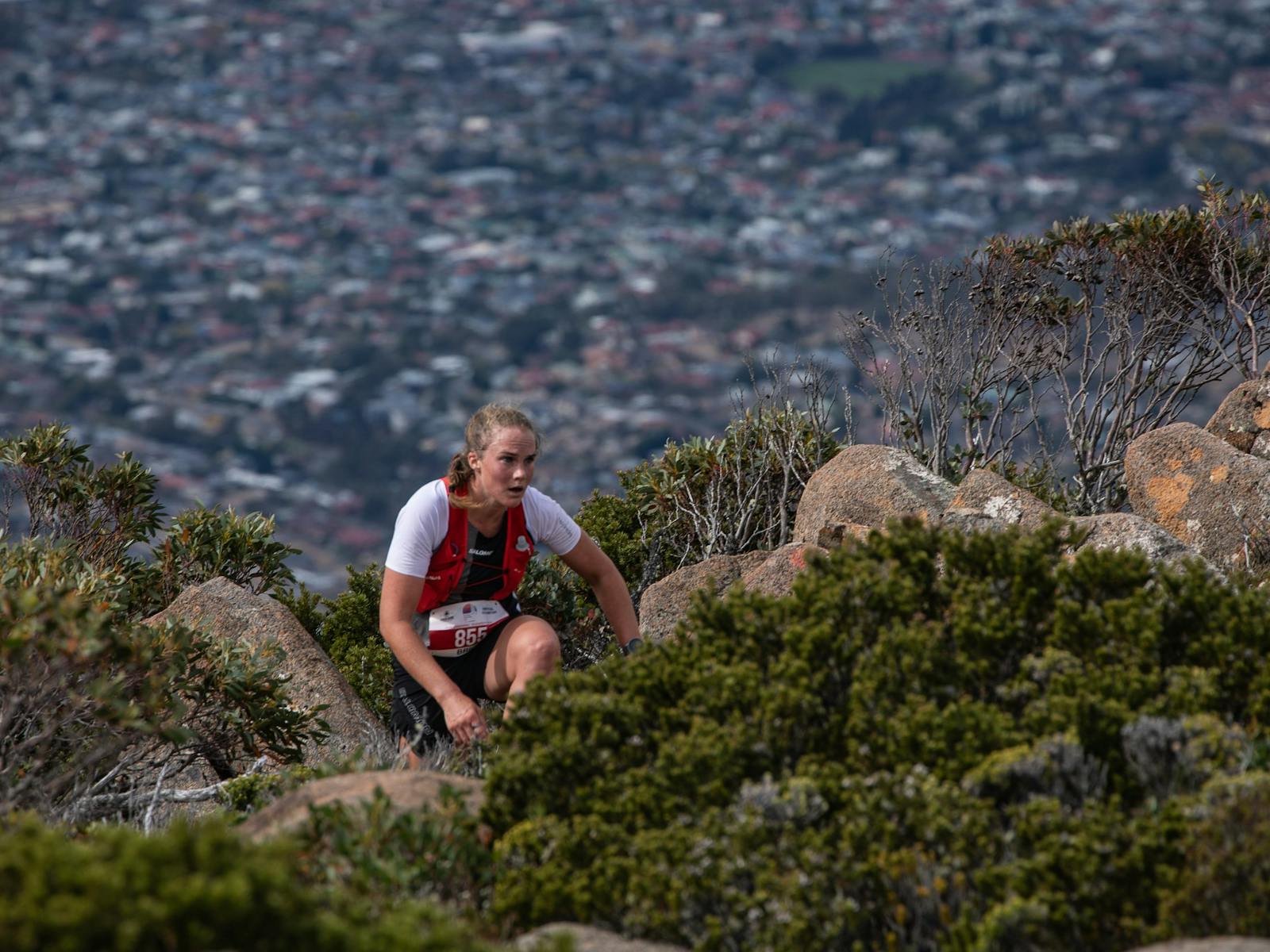 A runner navigates vegetation and rocks with Hobart in the background