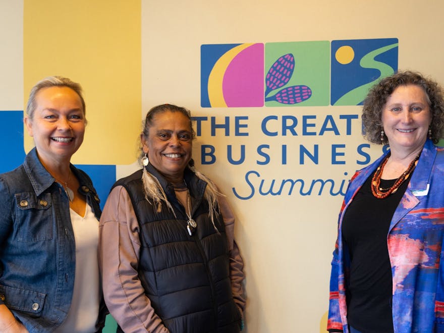 Three people including a First Nations elder infront of the event media wall